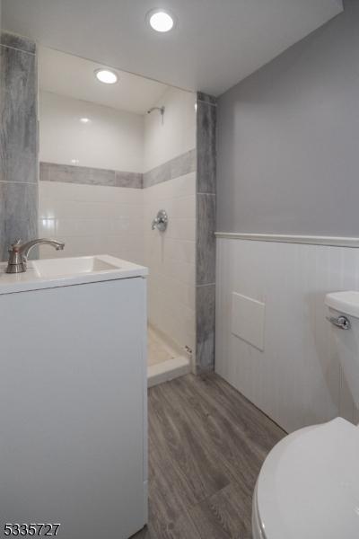 bathroom featuring hardwood / wood-style flooring, tiled shower, vanity, washer / dryer, and toilet