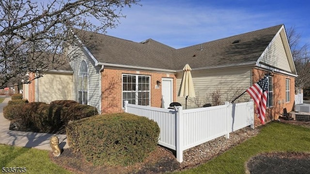 view of side of home with roof with shingles, fence, and brick siding