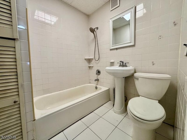 full bathroom featuring tiled shower / bath, tile walls, toilet, tile patterned floors, and a textured ceiling