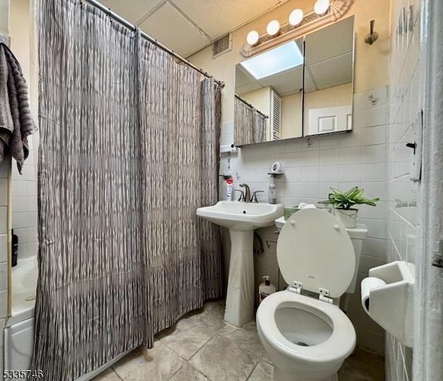 full bathroom with sink, shower / bath combo, tile walls, a drop ceiling, and toilet