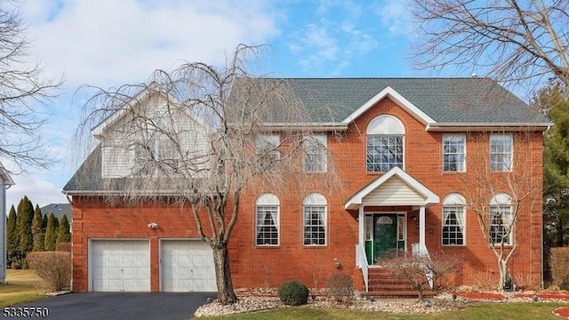 colonial home featuring an attached garage, roof with shingles, aphalt driveway, and brick siding