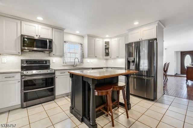 kitchen featuring sink, a breakfast bar area, white cabinetry, appliances with stainless steel finishes, and backsplash