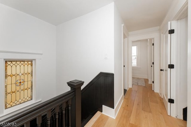 corridor with an upstairs landing, light wood-style flooring, and baseboards