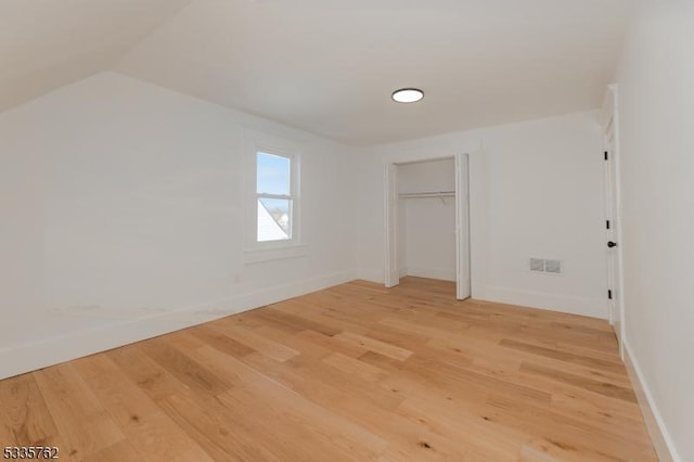 unfurnished bedroom featuring lofted ceiling, a closet, visible vents, wood finished floors, and baseboards