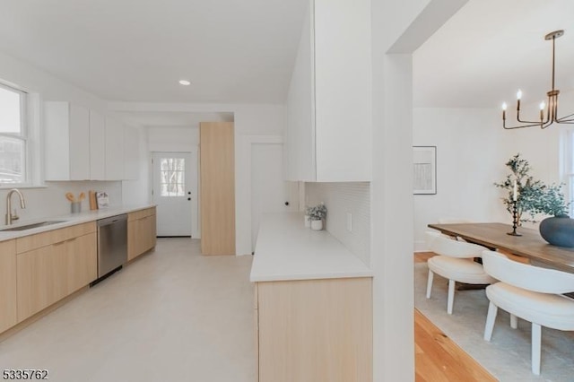 kitchen featuring light countertops, hanging light fixtures, stainless steel dishwasher, a sink, and modern cabinets