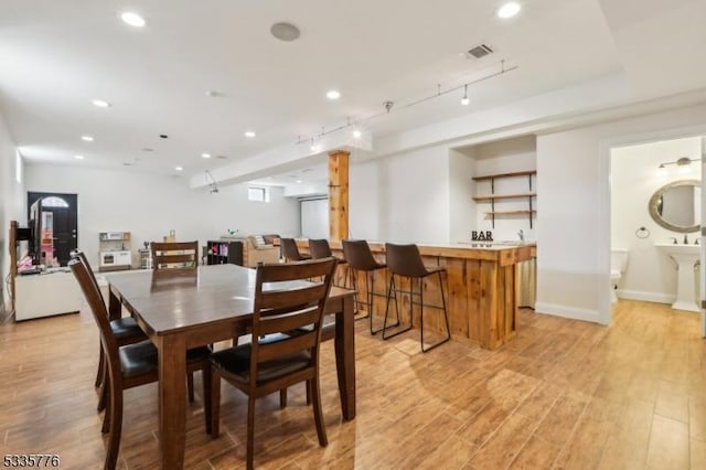 dining space with track lighting, bar, and light hardwood / wood-style flooring