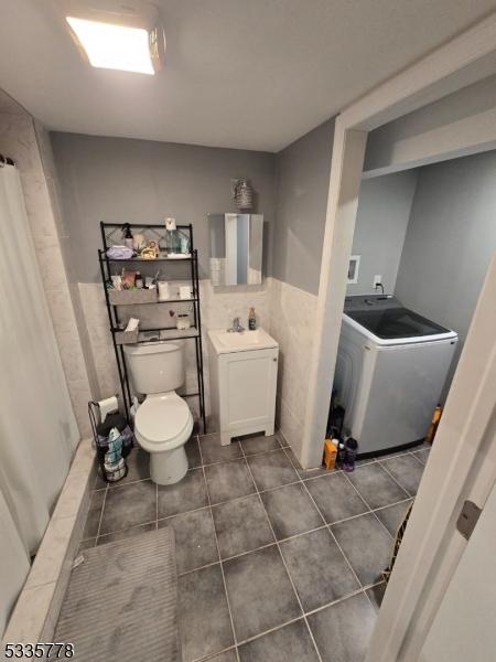 bathroom featuring tile patterned floors, toilet, tile walls, vanity, and washer / clothes dryer