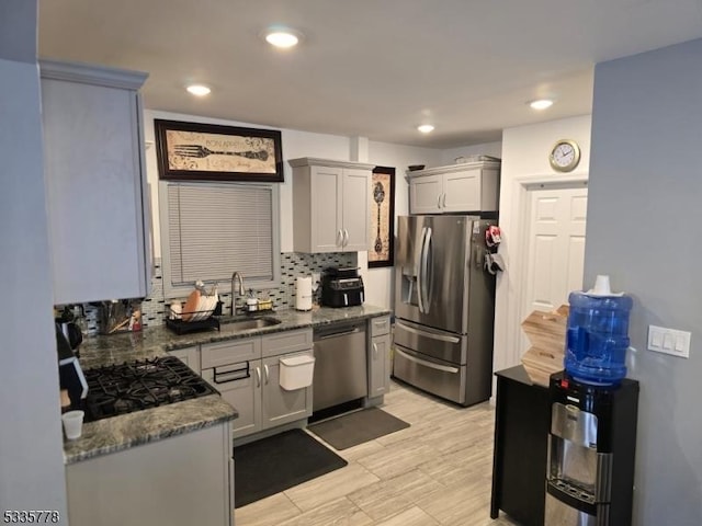 kitchen with sink, gray cabinetry, backsplash, stainless steel appliances, and dark stone counters