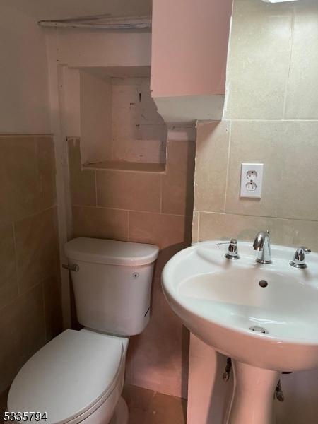 bathroom with toilet, sink, and tile walls