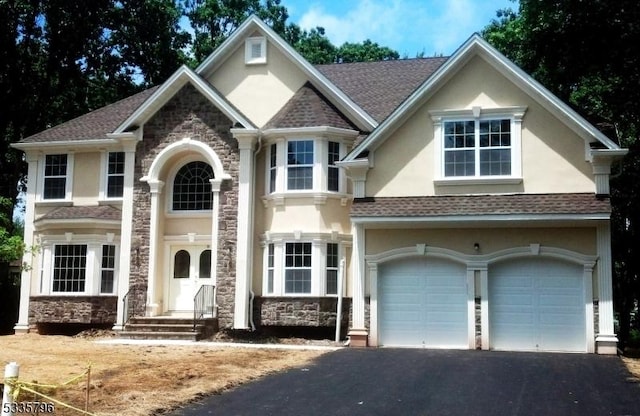 view of front facade with an attached garage, a shingled roof, stucco siding, stone siding, and driveway