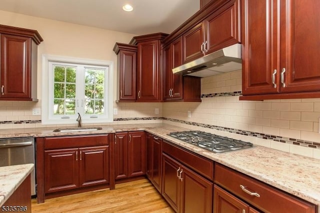 kitchen with light wood-style flooring, under cabinet range hood, a sink, stainless steel appliances, and light stone countertops