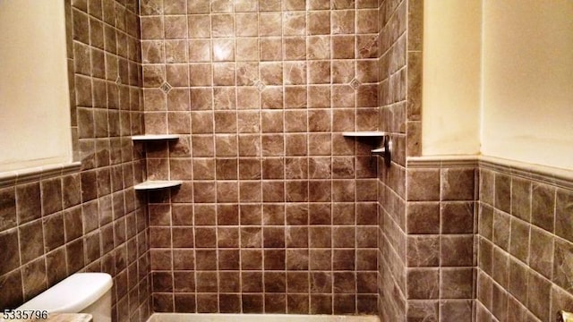 bathroom with tiled shower, toilet, tile walls, and wainscoting