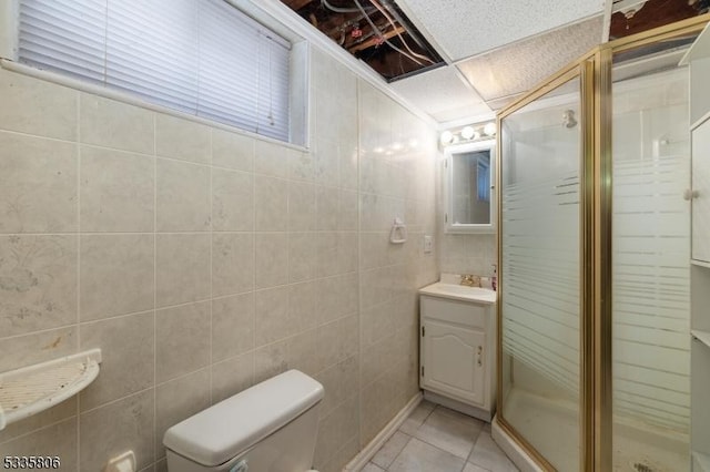 bathroom featuring a stall shower, toilet, tile patterned flooring, vanity, and tile walls