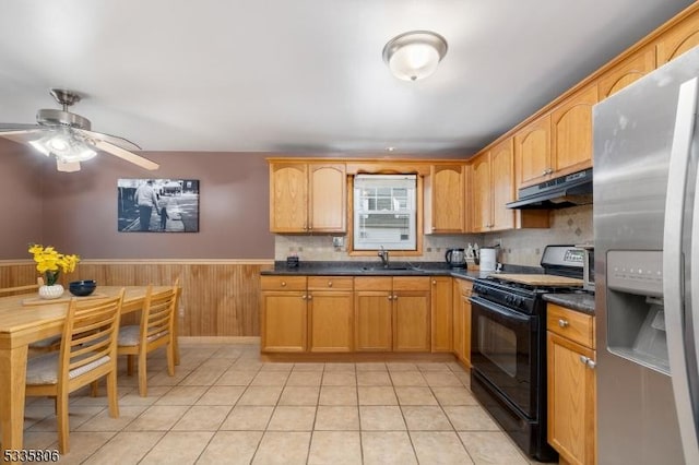 kitchen with stainless steel fridge, dark countertops, black range with gas stovetop, under cabinet range hood, and a sink