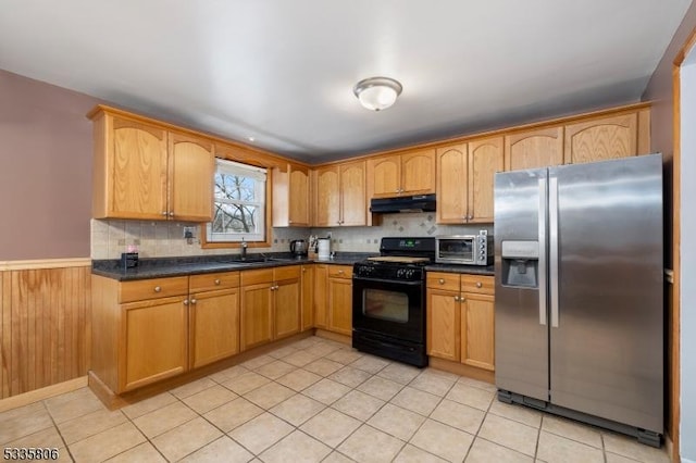 kitchen with under cabinet range hood, a sink, black gas stove, stainless steel refrigerator with ice dispenser, and dark countertops