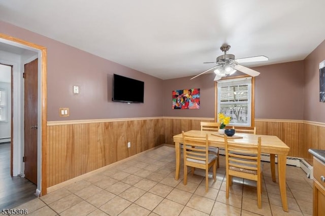 dining room featuring a wainscoted wall, baseboard heating, a ceiling fan, and wooden walls