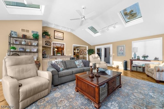 living room featuring ceiling fan, track lighting, lofted ceiling with skylight, and hardwood / wood-style floors