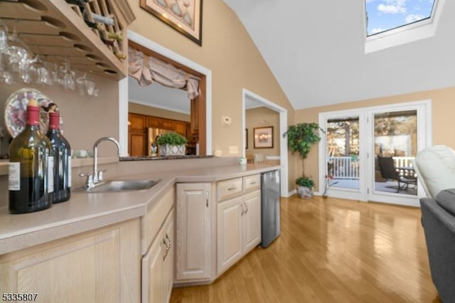 kitchen featuring lofted ceiling with skylight, sink, light brown cabinetry, and light hardwood / wood-style flooring