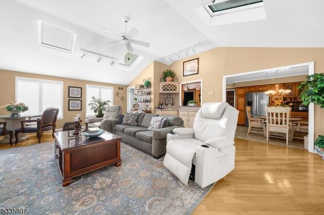 living room featuring track lighting, vaulted ceiling with skylight, ceiling fan with notable chandelier, and light wood-type flooring