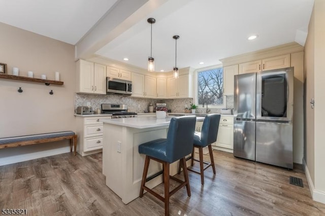 kitchen featuring appliances with stainless steel finishes, hanging light fixtures, a center island, wood-type flooring, and decorative backsplash