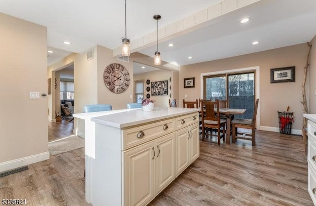 kitchen with beamed ceiling, hanging light fixtures, a center island, cream cabinets, and light hardwood / wood-style flooring