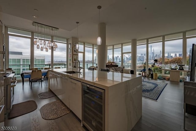 kitchen with decorative light fixtures, floor to ceiling windows, beverage cooler, and an island with sink