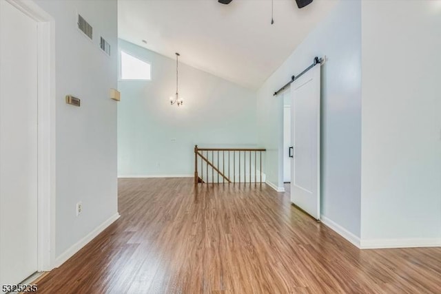 unfurnished room featuring hardwood / wood-style flooring, a barn door, ceiling fan with notable chandelier, and high vaulted ceiling