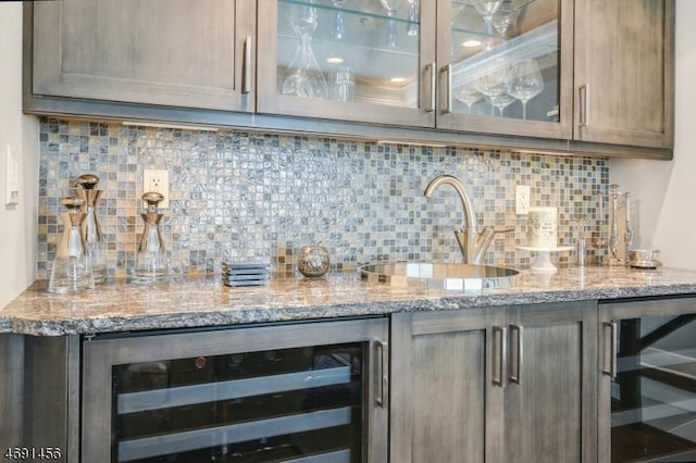 bar featuring light stone counters, beverage cooler, sink, and backsplash