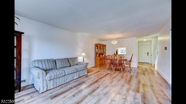 living room featuring a notable chandelier, a textured ceiling, and light hardwood / wood-style flooring