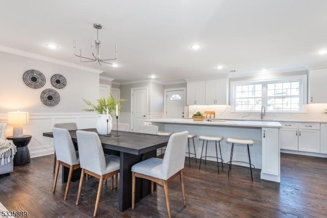 dining space with sink, a notable chandelier, ornamental molding, and dark hardwood / wood-style floors