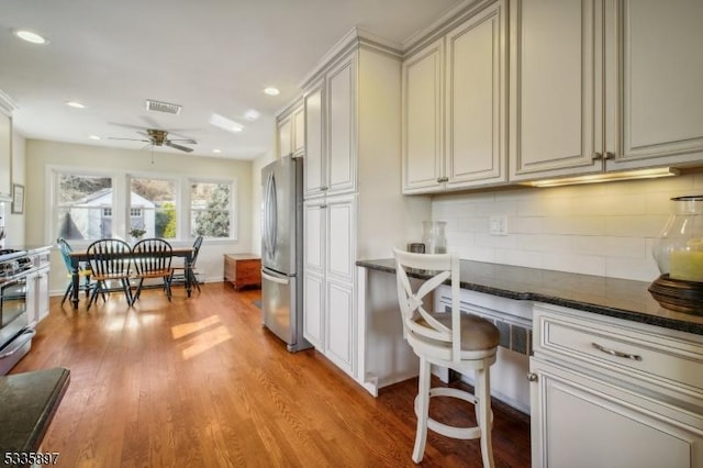 kitchen with dark stone countertops, stainless steel appliances, tasteful backsplash, built in desk, and light wood-type flooring