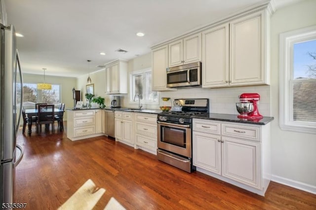 kitchen with dark hardwood / wood-style floors, decorative light fixtures, sink, kitchen peninsula, and stainless steel appliances