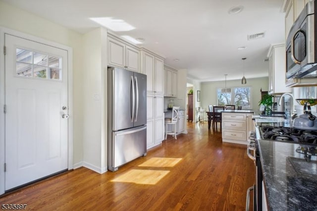 kitchen featuring hardwood / wood-style floors, decorative light fixtures, dark stone countertops, white cabinets, and stainless steel appliances