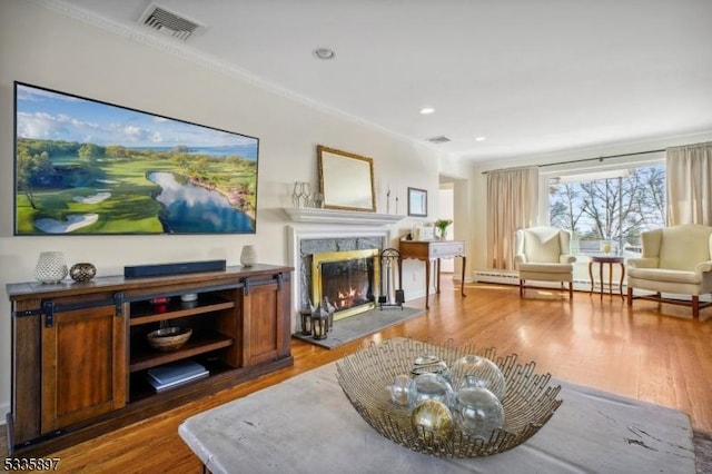 living room with hardwood / wood-style floors, a high end fireplace, ornamental molding, and a baseboard heating unit