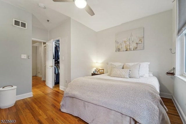 bedroom with lofted ceiling, wood-type flooring, a spacious closet, a closet, and ceiling fan