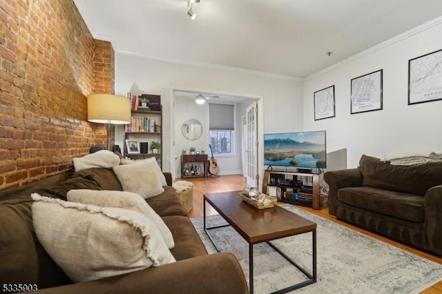 living room featuring wood-type flooring, ornamental molding, and brick wall