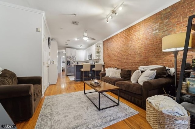 living room featuring crown molding, ceiling fan, brick wall, and light hardwood / wood-style floors