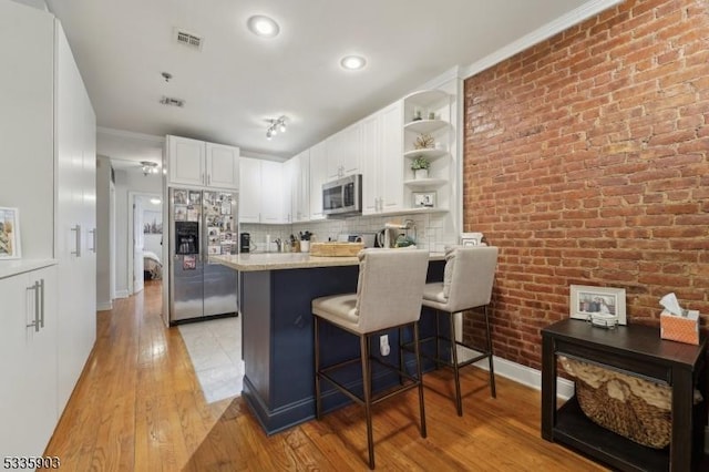 kitchen with a breakfast bar, appliances with stainless steel finishes, light hardwood / wood-style floors, white cabinets, and brick wall