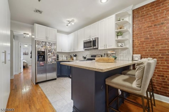 kitchen with backsplash, stainless steel appliances, blue cabinets, white cabinets, and a kitchen bar