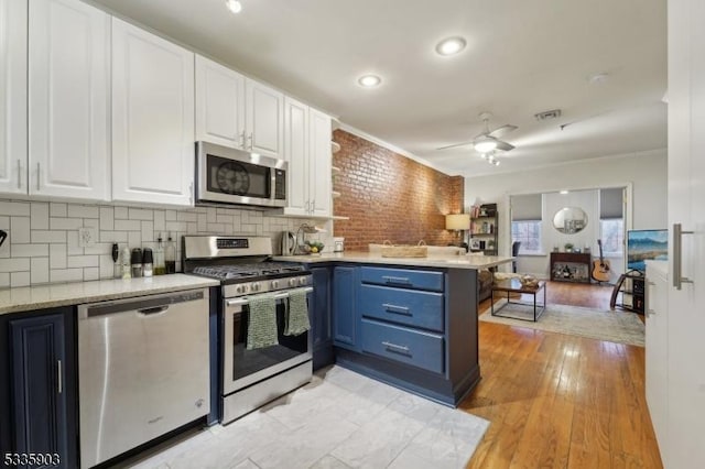 kitchen with appliances with stainless steel finishes, white cabinets, backsplash, kitchen peninsula, and light wood-type flooring