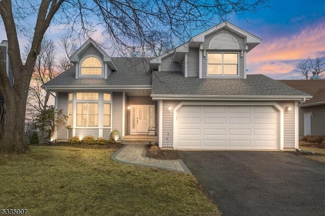 traditional home with driveway, a shingled roof, a garage, and a lawn