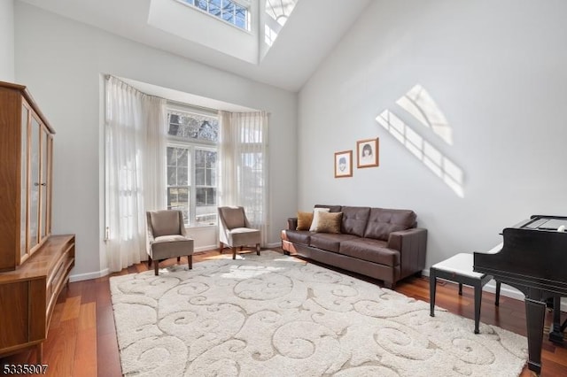 sitting room with high vaulted ceiling, a skylight, wood finished floors, and baseboards