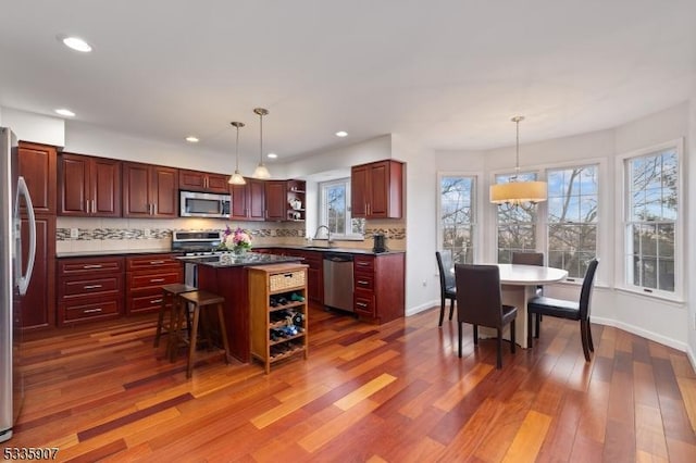 kitchen featuring open shelves, appliances with stainless steel finishes, a sink, dark brown cabinets, and wood finished floors