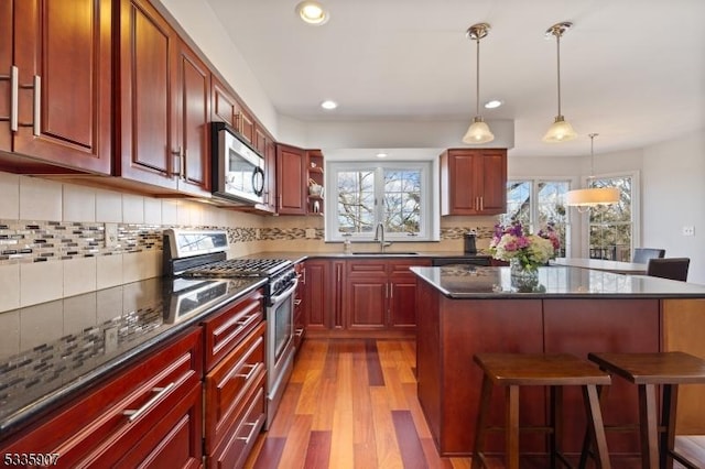 kitchen with light wood-style flooring, stainless steel appliances, a sink, a kitchen breakfast bar, and dark brown cabinets