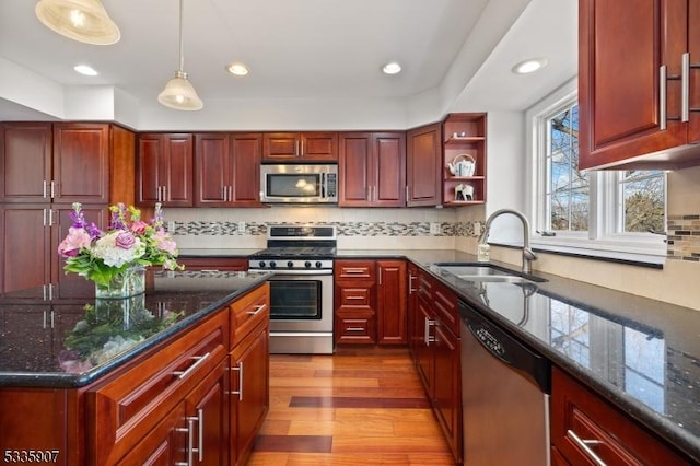 kitchen featuring appliances with stainless steel finishes, hanging light fixtures, dark brown cabinets, light wood-type flooring, and a sink