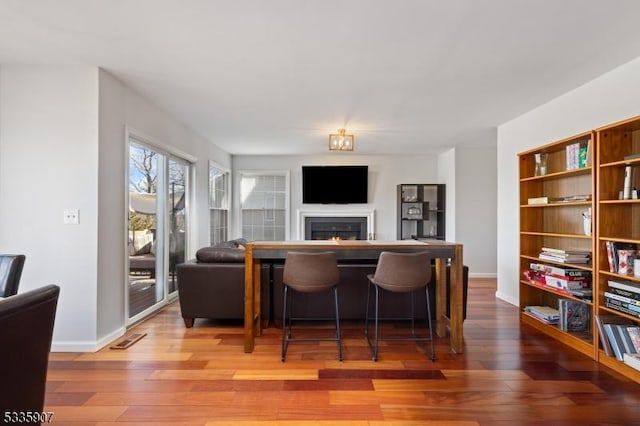 living area featuring a warm lit fireplace, wood-type flooring, visible vents, and baseboards