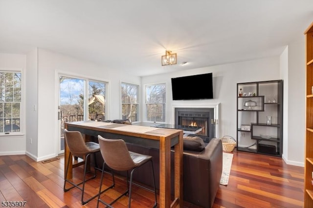 bar with a warm lit fireplace, baseboards, and dark wood finished floors