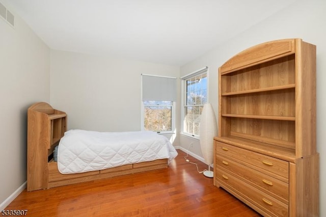 bedroom with baseboards, visible vents, and wood finished floors