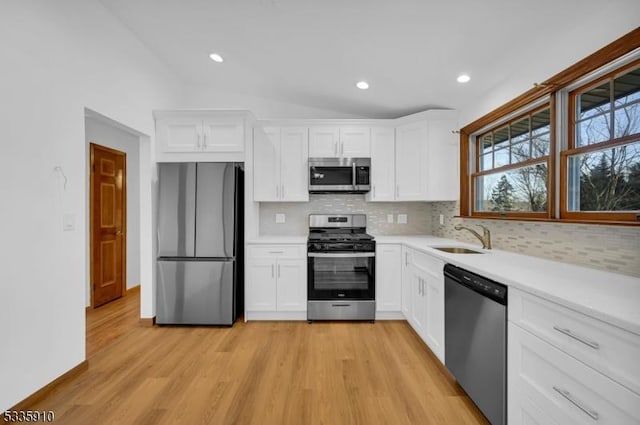 kitchen with sink, white cabinetry, vaulted ceiling, stainless steel appliances, and decorative backsplash