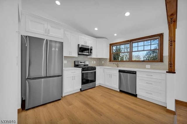 kitchen with lofted ceiling, light hardwood / wood-style flooring, white cabinetry, stainless steel appliances, and decorative backsplash